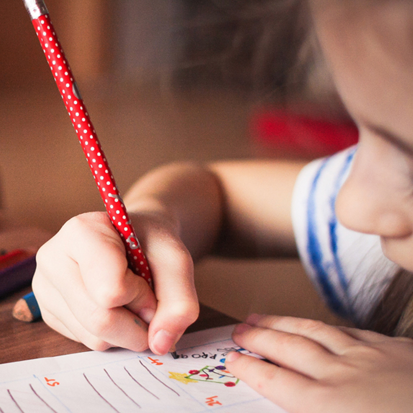 Up close image of a young girl holding a red pencil and colouring in.